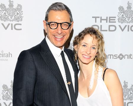 Hollywood actor Jeff Goldblum in a black suit and black tie poses a photo with wife Emilie Livingston.